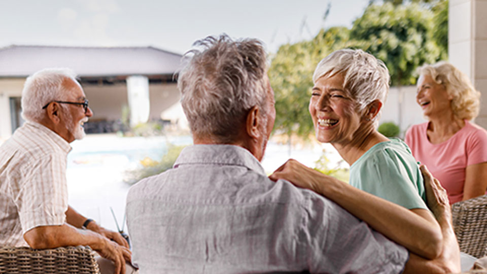 Group of male and female senior living residents at Mission Grove at Stoneybrook sitting outdoors on patio furniture